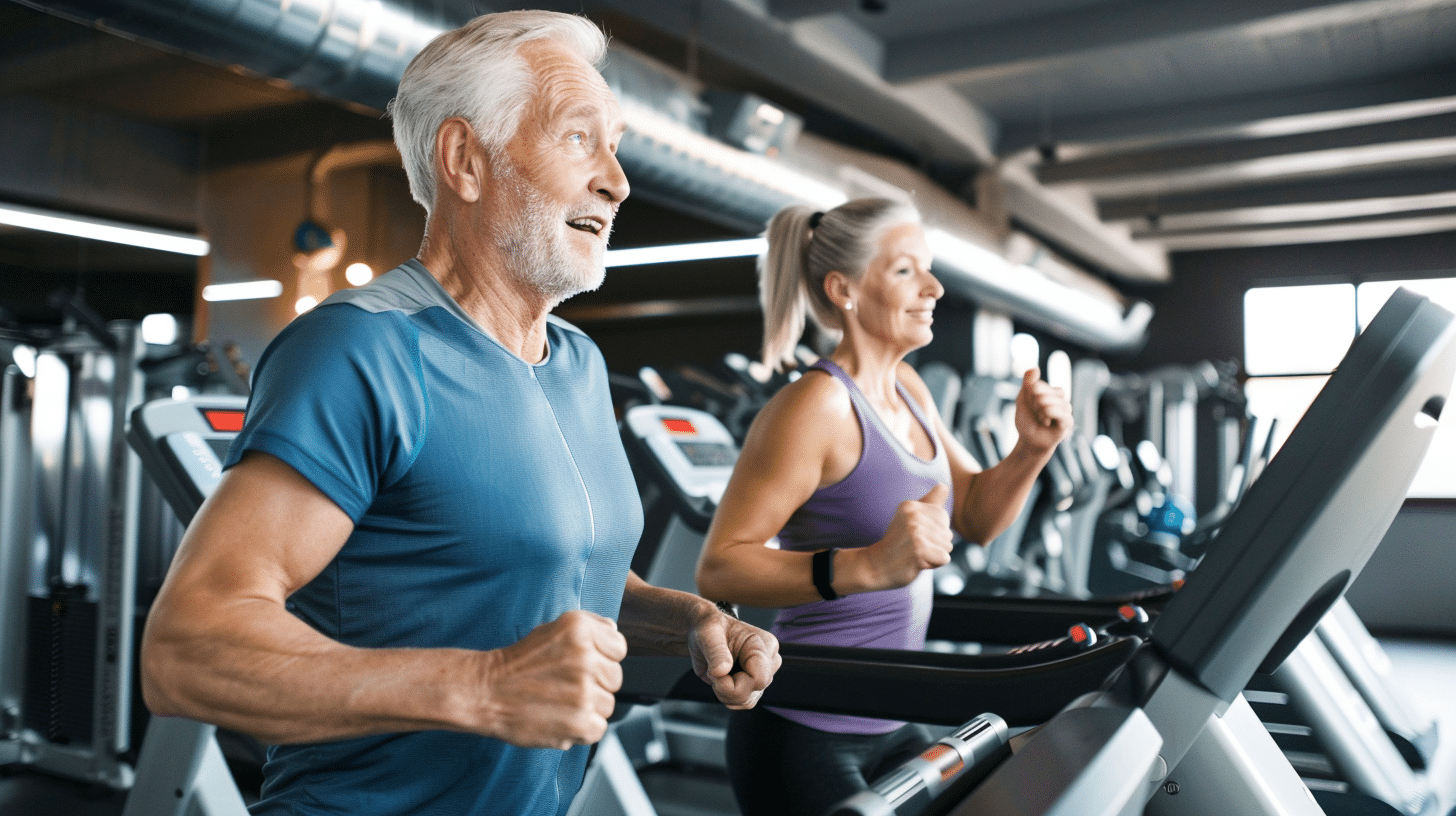 An image of a happy and healthy couple in their 60s engaged in running exercises on the treadmill inside a gym.